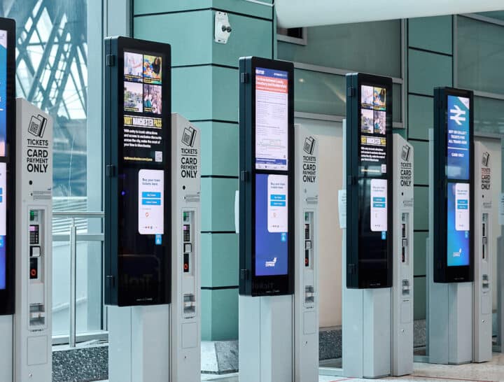 A row of modern, sleek ticket vending machines in a railway station, showcasing the intuitive touchscreen technology being rolled out to improve the passenger retail experience.