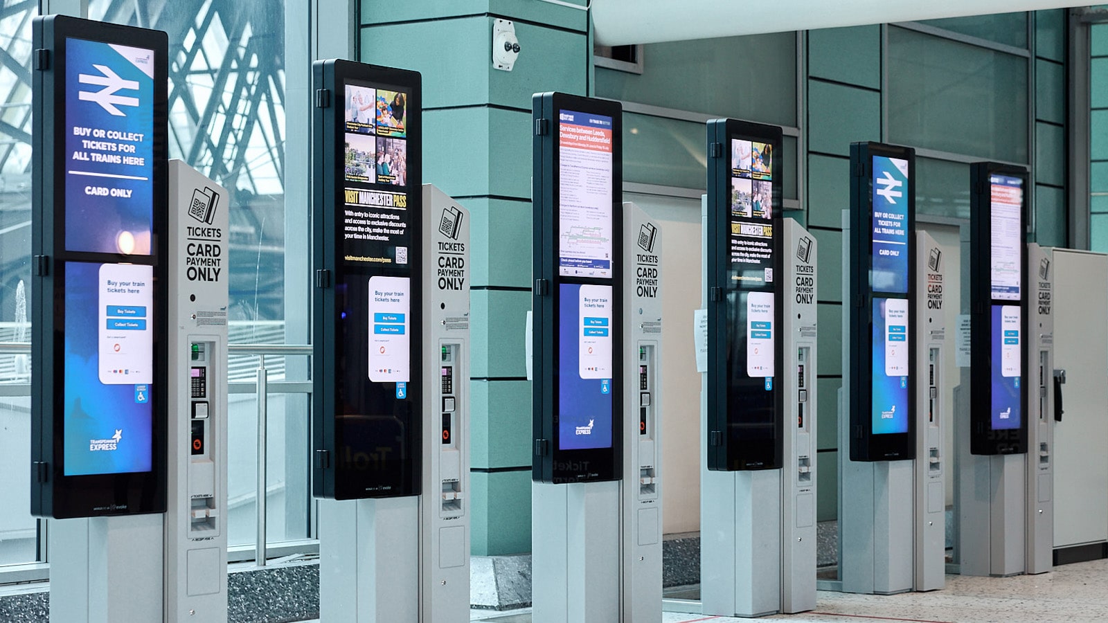 A row of modern, sleek ticket vending machines in a railway station, showcasing the intuitive touchscreen technology being rolled out to improve the passenger retail experience.