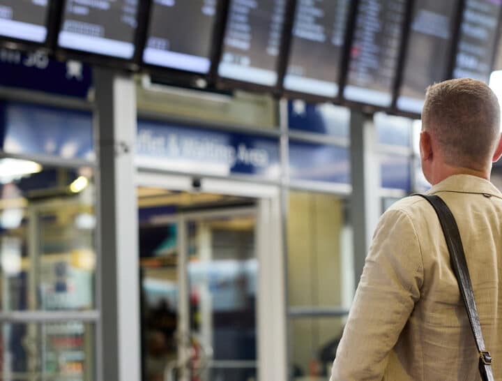 A passenger looking up at digital departure screens in a railway station, illustrating the critical role of timely and accurate information in the customer journey.