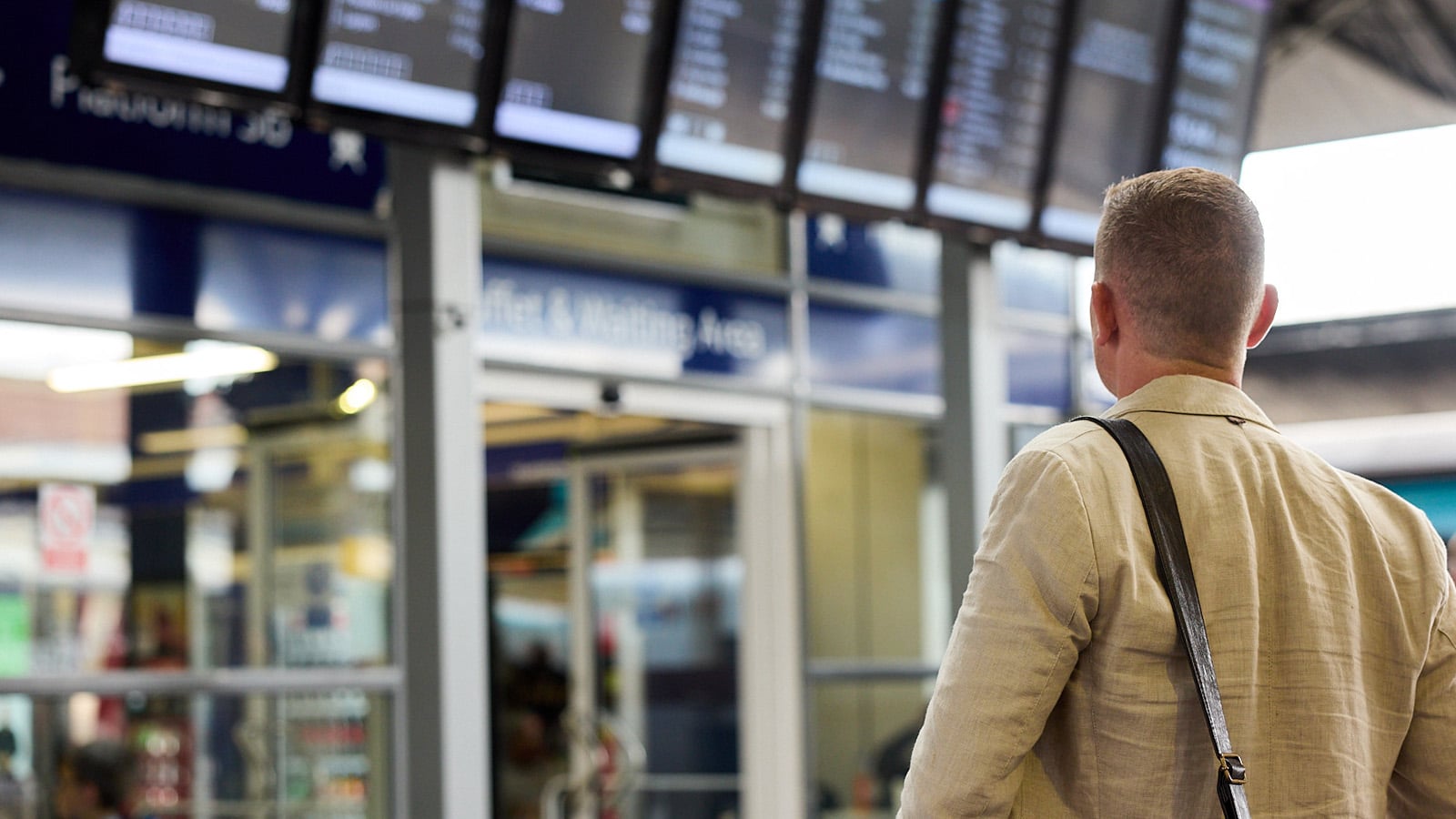 A passenger looking up at digital departure screens in a railway station, illustrating the critical role of timely and accurate information in the customer journey.